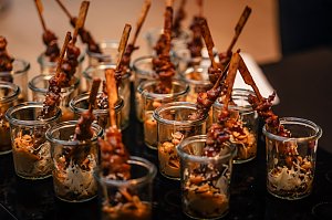 Mehrere kleine Gl&auml;ser gef&uuml;llt mit asiatisch anmutenden Snacks, darin marinierte Fleischspie&szlig;e mit Sesam und Beilage.