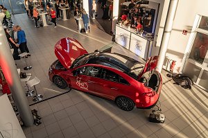 Von oben fotografierter roter Mercedes mit She�s Mercedes-Logo, Motorhaube und Kofferraum ge&ouml;ffnet. Im Autohaus sind Besucher an Stehtischen und einem Catering-Stand zu sehen. Mercedes-Benz CLA 250+ mit EQ-Technologie | Energieverbrauch kombiniert: 14,1-12,2 kWh/100 km | CO2Emissionen kombiniert: 0 g/km | CO2-Emissionsklasse: A