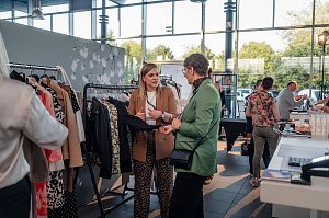 Zwei Frauen unterhalten sich an einem Kleiderst&auml;nder mit verschiedenen Jacken und Blusen. Die Frau links tr&auml;gt einen braunen Blazer, die Frau rechts einen gr&uuml;nen Blazer.