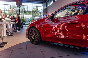 Seitliche Nahaufnahme eines roten Mercedes mit She�s Mercedes-Logo, im Hintergrund Menschen an Stehtischen im Autohaus. Mercedes-Benz CLA 250+ mit EQ-Technologie | Energieverbrauch kombiniert: 14,1-12,2 kWh/100 km | CO2Emissionen kombiniert: 0 g/km | CO2-Emissionsklasse: A