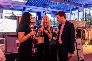 Drei Personen, darunter Christina Dost, ziehen Lose aus einem goldenen Hut, zwei halten Mikrofone, im Hintergrund ein Bildschirm mit She�s Mercedes Ladies Night und Kleidungsst&auml;nder.