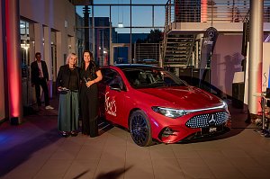 Zwei Frauen, darunter Christina Dost, posieren neben einem roten Mercedes mit She�s Mercedes-Logo, im Hintergrund eine Treppe und weitere G&auml;ste.
