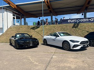 Zwei Mercedes-Benz Cabriolets, eines schwarz und eines weiß, stehen nebeneinander auf einem befestigten Platz beim Leichtathletik-Meeting Anhalt 2025. Hinter den Fahrzeugen verläuft ein Grashang mit Zuschauern und einer überdachten Tribüne.