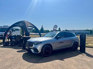 Ein silberner Mercedes-Benz SUV des Autohauses Peter steht während des Leichtathletik-Meetings Anhalt 2025 an einer mobilen Ladesäule. Links befindet sich ein schwarzes Promotion-Zelt mit dem Schriftzug �Jetzt Probe fahren�, daneben mehrere Boxen und Mitarbeiter des Autohauses. Im Hintergrund sind Wohnmobile, Bäume und ein sonniger, klarer Himmel zu sehen.