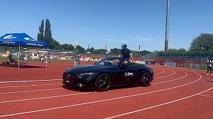 Ein schwarzes Mercedes-AMG Cabrio des Autohauses Peter fährt mit einem Sportler über die Laufbahn im Stadion des Anhalt 2025 Leichtathletik-Meetings. Im Hintergrund sind das blaue Zelt der Stadtwerke Dessau, einige Zuschauer und die Beschilderung mit �WELCOME� und �BIENVENUE� zu sehen.