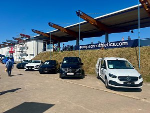 Mehrere Mercedes-Benz Fahrzeuge, präsentiert vom Autohaus Peter, stehen aufgereiht am Rand des Stadions beim Anhalt 2025 Leichtathletik-Meeting. Unter den ausgestellten Autos sind ein weißer eCitan, ein schwarzer EQV und weitere Mercedes-Modelle zu sehen. Im Hintergrund befinden sich Zuschauertribünen, ein Banner mit der Aufschrift �european-athletics.com� und einige Besucher auf dem Gelände.