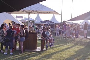 Besucher genießen den Abend auf der Wiese beim Reitturnier in Immenrode. Unter großen Sonnenschirmen und Pagodenzelten stehen Gruppen zusammen, einige Gäste sitzen an Stehtischen oder auf Bänken.