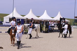 Mehrere Kinder reiten auf Ponys beim Reitturnier in Immenrode, begleitet von Erwachsenen in Reitkleidung. Im Hintergrund stehen weiße Pagodenzelte und ein Hindernis mit Mercedes-Benz-Werbung.