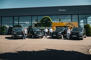 Vor einem modernen Autohaus mit dem Namen Peter stehen vier schwarze Opel-Transporter in einer Reihe. Vier Personen � drei Männer und eine Frau � posieren jeweils neben den Fahrzeugen. An der Glasfassade ist das Opel-Logo und ein gelber Hintergrund zu sehen.