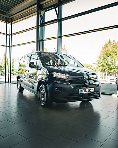 Ein schwarzer Opel-Transporter steht in einem hellen Autohaus mit großen Glasfenstern.