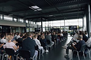 Blick von hinten in die Veranstaltungshalle: Zahlreiche Auszubildende und ihre Eltern sitzen in Reihen und verfolgen die Begrüßung der Autohaus-Peter-Gruppe.