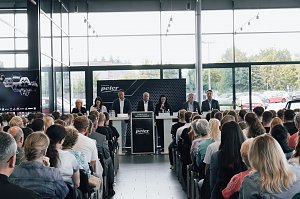 Blick auf das Podium mit der Geschäftsführung und Ausbildungsleitung der Autohaus-Peter-Gruppe. Dahinter große Fensterfront, davor sitzen die neuen Auszubildenden und Gäste.