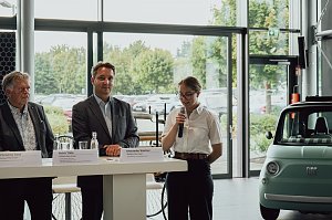 Lilly Hecker steht am Rednerpult mit einem Mikrofon und spricht zu den neuen Auszubildenden. Neben ihr stehen Mitglieder der Gesch&auml;ftsf&uuml;hrung der Autohaus-Peter-Gruppe.