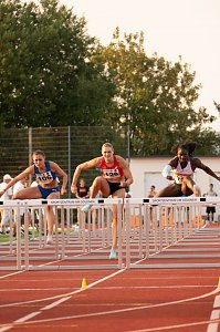 Drei Athletinnen im Hürdenlauf springen gleichzeitig über eine Hürde auf der roten Tartanbahn. Im Vordergrund sind die Hürden mit der Aufschrift �Sportzentrum am Göldner� zu sehen. Zuschauer und Kampfrichter im Hintergrund.