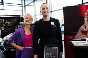 Eine Frau (Moderatorin Mandy Kossira) in lila Blazer und pinkem Top steht neben einem Mann im schwarzen Anzug. Beide l&auml;cheln. Neben ihnen ein Aufsteller mit der Aufschrift Mein Fischer.