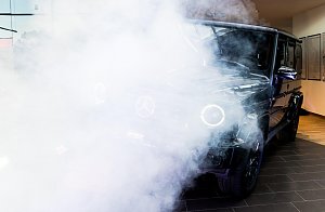 Eine schwarze Mercedes G-Klasse wird in Szene gesetzt. Dichter wei&szlig;er Nebel und Scheinwerferlicht verdecken teilweise das Auto.