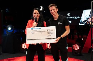 Christina Dost im roten Blazer und ein junger Mann im schwarzen Autohaus-Peter-Shirt pr&auml;sentieren einen &uuml;bergro&szlig;en Spendenscheck der Volksbank &uuml;ber 1.450 Euro.