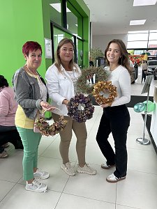 Drei Frauen stehen im Autohaus Autowelt Peter und halten selbstgemachte herbstliche Kränze in den Händen. Im Hintergrund sind weitere Gäste und grüne Luftballons zur Feier von 130 Jahren �koda zu sehen.