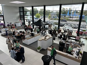 Blick von oben in den hellen Ausstellungsraum des Autohauses Autowelt Peter während der Feier zu 130 Jahren �koda. Besucherinnen und Besucher sitzen an Tischen, basteln und stricken, andere informieren sich an Ständen, darunter ein SCOTT-Zelt mit Fahrrädern.