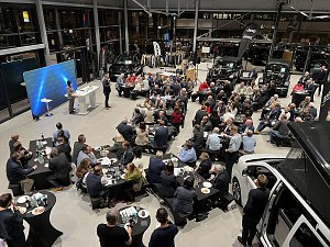 Blick von oben auf die Veranstaltung: zahlreiche Tische mit G&auml;sten, die dem CDU-Wirtschaftsdialog folgen. Die B&uuml;hne steht links mit zwei Rednern, im Hintergrund mehrere Autos und Firmenbanner von Jeep und Dodge.