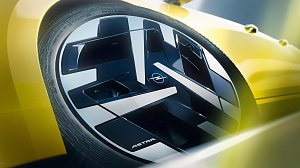 Detailaufnahme einer Fahrzeugfelge mit einem geometrisch gestalteten, schwarz-silbernen Felgendesign. In der Mitte befindet sich das Opel-Logo. Am unteren Rand des Felgenblatts steht ASTRA. Das gelbe Fahrzeugheck ist im Hintergrund unscharf zu erkennen, akzentuiert durch weiche Lichteff