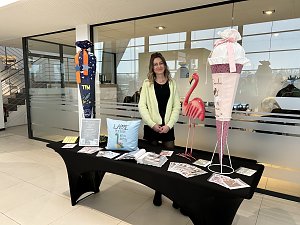 Frau steht hinter einem Infotisch mit Deko und Flyern, daneben große Schultüte und Flamingo-Figur im Autohaus.