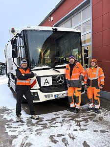 Zwei Mitarbeiter und unser Verkaufsberater André Schmidt in orangefarbener Schutzkleidung stehen vor einem Müllfahrzeug im Schnee auf einem Betriebshof.