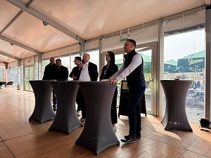 6 Personen stehen an mehreren Stehtischen, einer davon spricht ins Mikrofon.
