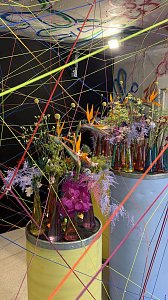 Kunstvoll inszenierte Blumenarrangements und viele bunte, durch den Raum gespannte Bindfäden.