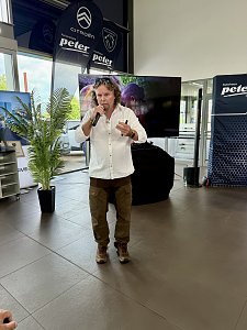 Eine Person steht vorn und spricht ins Mikrofon, im Hintergrund ein Bildschirm.