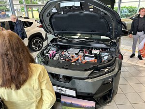 Subaru mit ge&ouml;ffneter Motorhaube und interessierten Personen, die hinein schauen.


