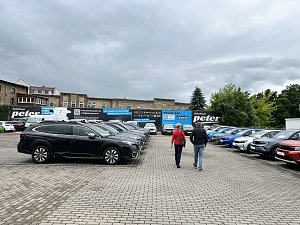 Hinterhof des Autohauses mit 2 schlendernden Personen, die sich die Fahrzeuge anschauen.

