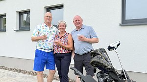 Drei Gäste stehen mit Getränken neben einem Golftrolley vor dem Clubhaus.
