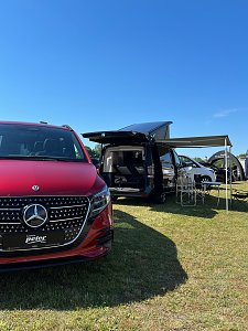 Ein roter Mercedes-Benz EQV im Vordergrund sowie eine schwarze V-Klasse Marco Polo mit ausgefahrenem Aufstelldach und Markise.