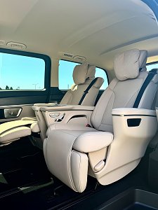 Der luxuri&ouml;se Innenraum einer Mercedes-Benz V-Klasse mit hellen Einzelsitzen und ausgefahrenen Fu&szlig;st&uuml;tzen.