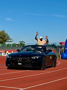 Ein Top-Athlet winkt dem Publikum w&auml;hrend der traditionellen Einfahrt aus einem schwarzen Mercedes-AMG SL Cabrio des Autohauses Peter auf der Laufbahn zu.