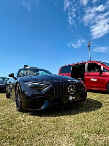 Ein sportliches schwarzes Mercedes-AMG SL Cabriolet und eine rote V-Klasse des Autohauses Peter pr&auml;sentieren sich nebeneinander auf der Ausstellungsfl&auml;che unter blauem Himmel.