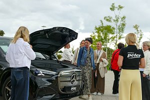 Eine Gruppe von Frauen, die sich im Freien um einen schwarzen Mercedes-Benz GLC mit geöffnetem Frunk versammelt haben und das Fahrzeug betrachten.
