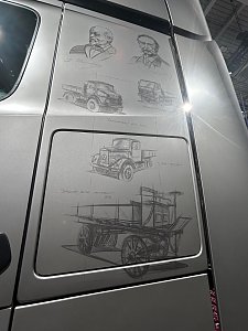 Silberne Lkw-Seitenwand mit feinen Zeichnungen. Oben sind Porträts von Carl Benz und Gottlieb Daimler. Darunter sind verschiedene historische Lastwagen skizziert, vom hölzernen Ur-Modell bis zum moderneren Hauben-Lkw.