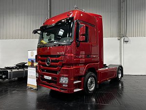 Dunkelroter Mercedes-Benz Actros Lkw schräg von vorne in einer Halle. Das fahrbereite Fahrerhaus glänzt im Scheinwerferlicht. Hinten ist das freie Fahrgestell ohne Auflieger zu sehen.