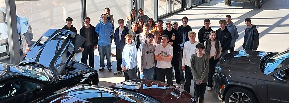 "Gruppe von Jugendlichen steht im Ausstellungsraum des Autohauses Peter zwischen mehreren Fahrzeugen mit ge&ouml;ffneten Motorhauben. Aufnahme im Rahmen des Girls & Boys Day 2025, Sonnenlicht f&auml;llt durch gro&szlig;e Glasfronten ins Geb&auml;ude.