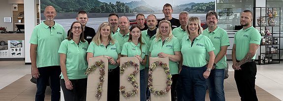 Teamfoto der Skoda Crew in &uuml;berwiegend t&uuml;rkisfarbenen T-Shirts; devor eine 130 aus gebundenen Blumen.