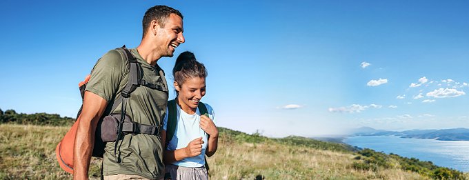 Wanderpaar mit Rucks&auml;cken l&auml;uft bei Sonnenschein durch K&uuml;stenlandschaft.
